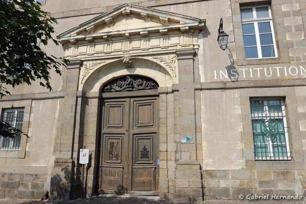 Dans la rue du collège, le beau portail de l'ancien hôtel de Plouër, orné de pilastre, d'un mascaron, d'un fronton en pierres calcaire et des enroulements sculptés dans le tympan (Saint-Malo, mai 2023)