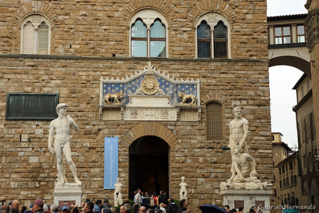 Entrée du Palazzo Vecchio, encadrée par une copie du David de Michel Ange et Hercaule et Cactus de Baccio Bandinelli, avec en haut à droite, le corridor de Vasari (Florence, Italie,
